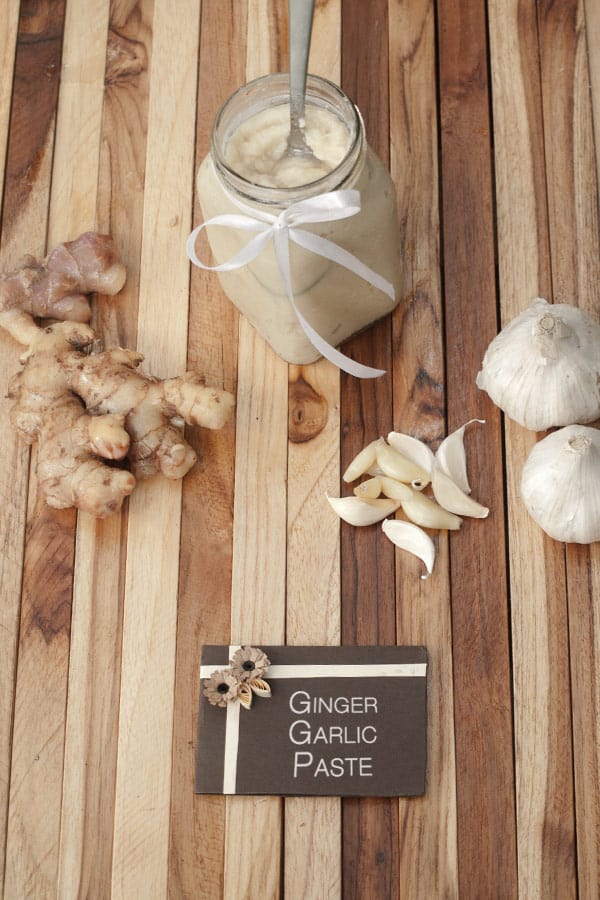 a card with ginger and garlic written on it and fresh unpeeled ginger and peeled garlic and ginger garlic paste in a jar with a wooden background